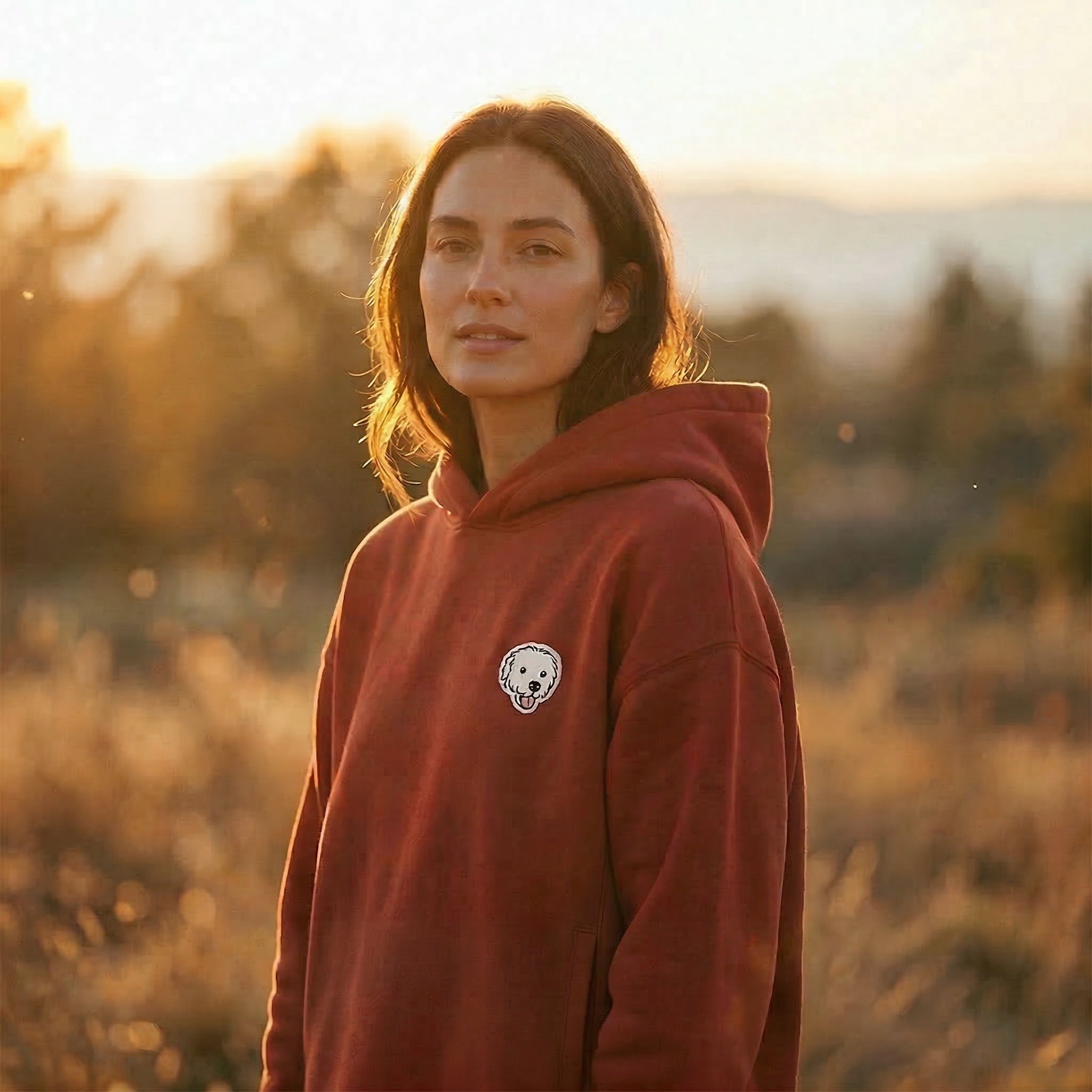 Woman wearing a wine hoodie with a logo in a field at sunset